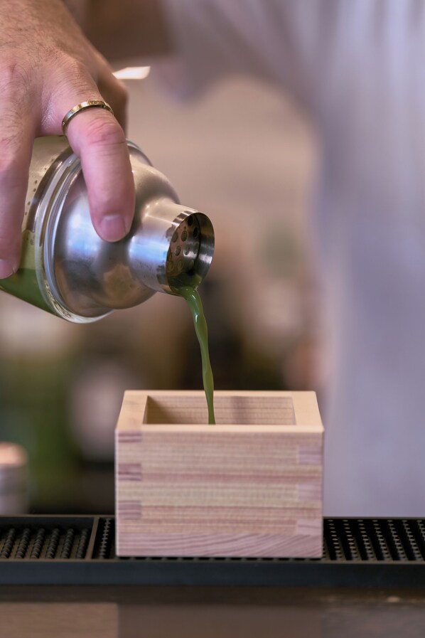 A hand pouring a green liquid from a metallic container into a wooden box. - Ayanishiki Gion (Kyoto)