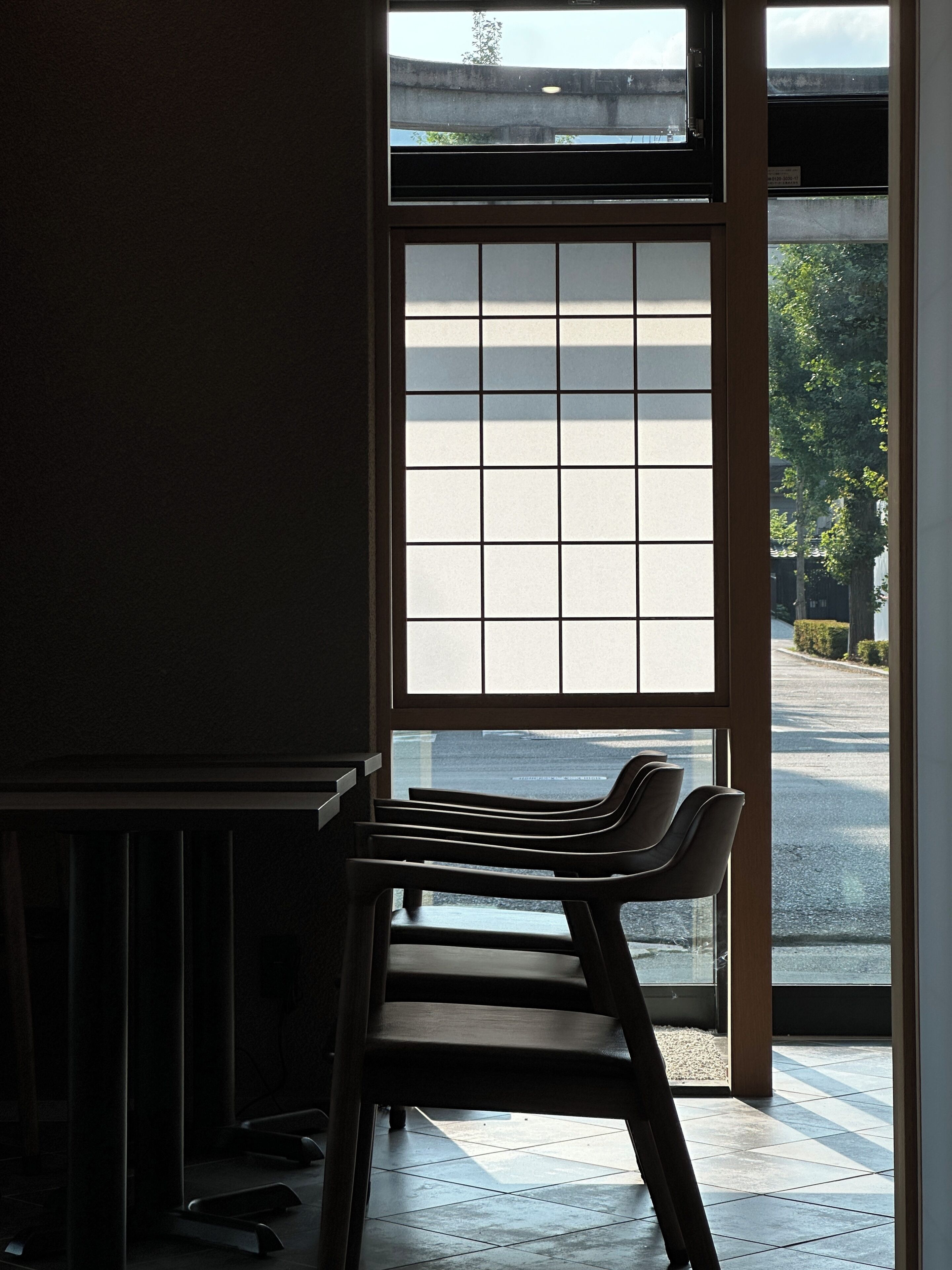 Una habitación con vistas a través de una ventana, una silla y piso de baldosas.