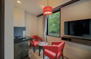 A hotel room with a TV, a desk with a laptop, a small table with two chairs, and a window with a view of trees. - Ayanishiki Gion (Kyoto)