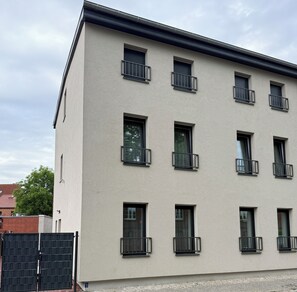 Ein mehrgeschossiges Gebäude mit einer glatten Fassade, zahlreichen Fenstern mit schwarzen Geländern und einer sichtbaren Tür.