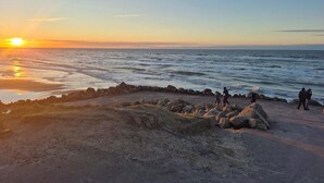 Een strand met een rotsenrijke golfbreker, een kalme zee en een zonsondergang.