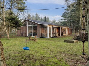 A wooden cabin with a glass extension, surrounded by a grassy yard and trees. - 4 Star Holiday Home in Lokken (Lokken)