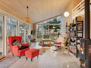 Ein gemütliches Wohnzimmer mit Kamin, Bücherregal und großem Fenster mit Blick auf einen Garten.