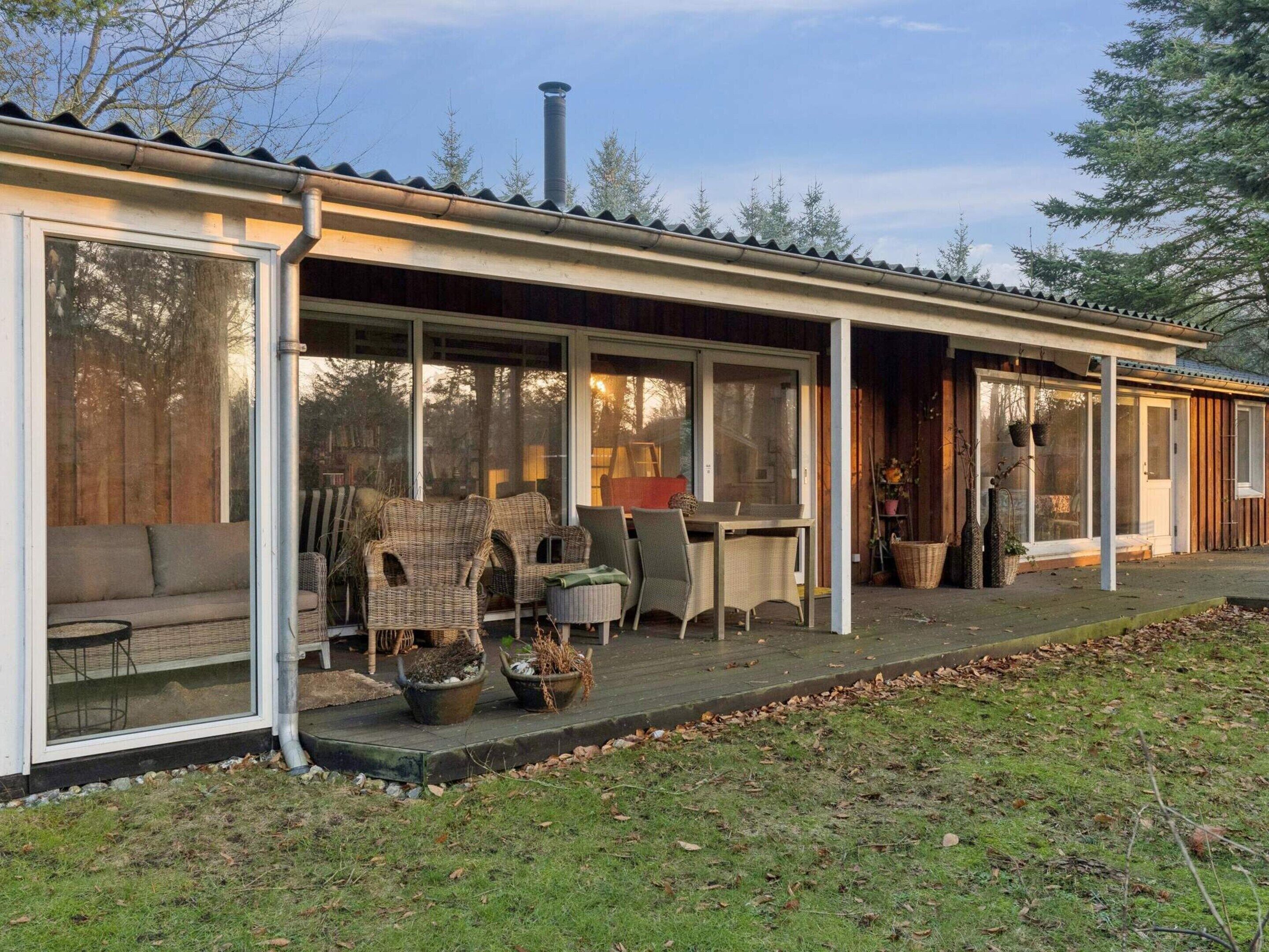 Een overdekt terras met rieten meubels, een tafel en stoelen, en een houten deur die naar binnen leidt.