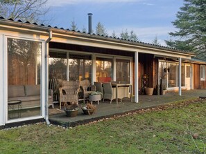A covered outdoor seating area with wicker furniture, a table, and chairs, and a wooden door leading to the interior. - 4 Star Holiday Home in Lokken (Lokken)