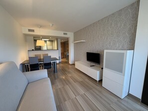 Ein modernes Wohnzimmer mit Sofa, Fernseher, Essbereich und einer Küche im Hintergrund.