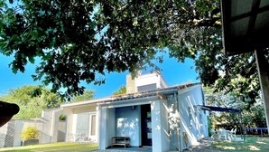 Um pequeno edifício térreo com varanda coberta, entrada por um caminho de cascalho e céu azul no fundo.