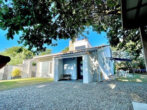 A small, single-story building with a covered porch, a gravel driveway, and a clear blue sky in the background.