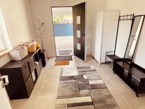 A hallway with a tiled floor, a door leading outside, a black bench, a mirror, and a wall-mounted rack.