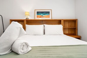 A neatly made bed with white linens, a rolled white towel, and a framed painting above the headboard. - Edmund Place – Charming Fremantle Retreat (Fremantle)