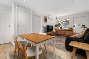 A modern living room with a wooden dining table, white chairs, a black sofa, and a TV. - Edmund Place – Charming Fremantle Retreat (Fremantle)