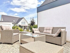 An outdoor patio area with wicker furniture, a glass table, and a view of a house in the background. - Country house 150m², yurt and brazier (Wingersheim les Quatre Bans)