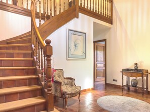 A wooden staircase with a railing, a patterned armchair, a framed artwork on the wall, and a tiled floor. - Country house 150m², yurt and brazier (Wingersheim les Quatre Bans)