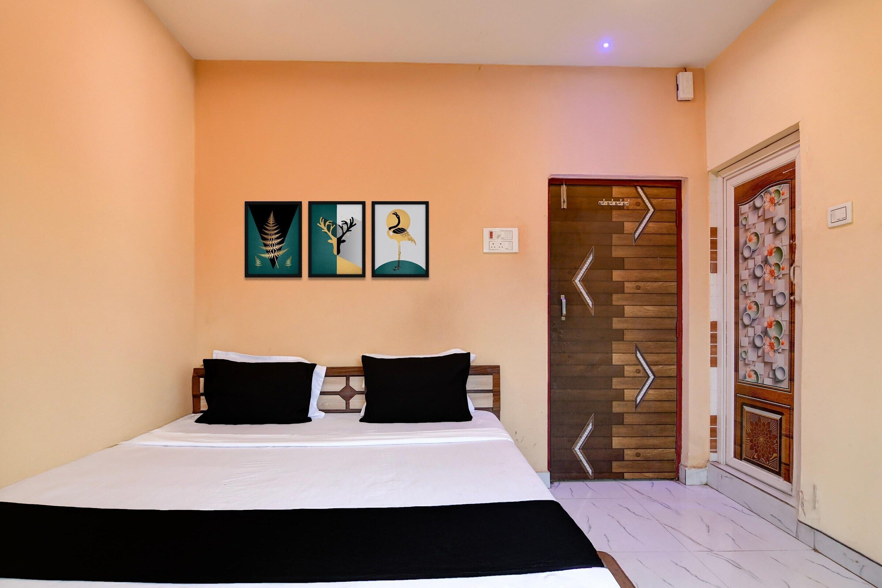 A bedroom with a bed, two black pillows, and three framed artworks on the wall.