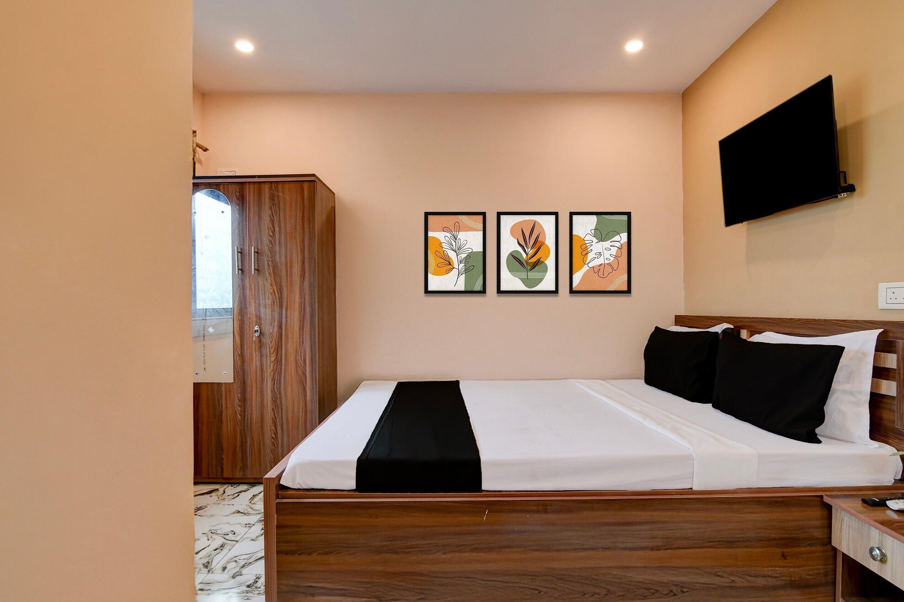 Une chambre à coucher avec un lit en bois, une armoire, un téléviseur à écran plat et trois œuvres d’art encadrées accrochées au mur.