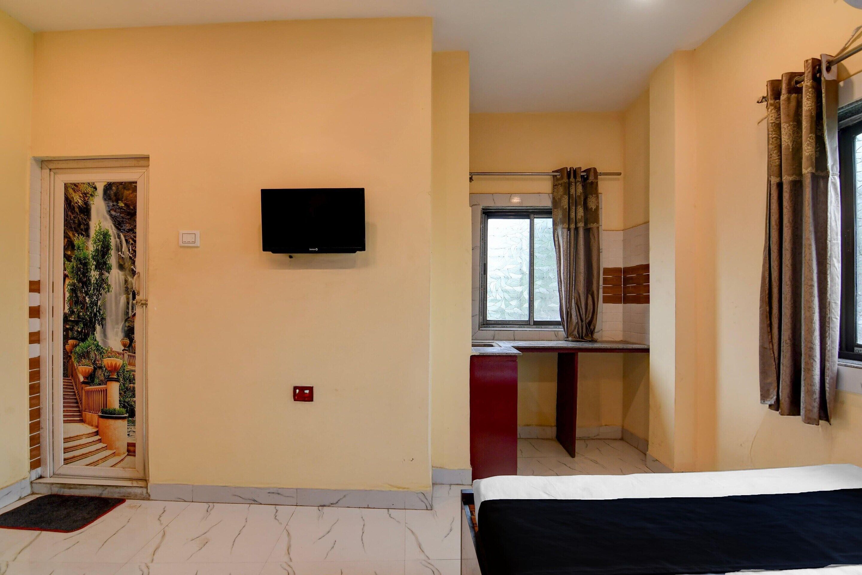 Ein Zimmer mit einem Bett, einem Fernseher, einem Fenster mit Vorhängen, einem kleinen Schreibtisch und einem Badezimmer mit Dusche.