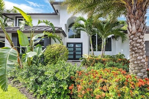 Ein modernes Haus mit weißer Fassade, großen Fenstern und einem gepflegten Garten mit verschiedenen Pflanzen und Blumen.