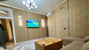 Una sala de estar moderna con una mesa de centro de madera, un sofá grande, un tapete redondo y un televisor de pantalla plana montado en la pared.