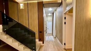 Un interior moderno con una escalera de cristal, suelo de madera y un pasillo que conduce a una puerta.