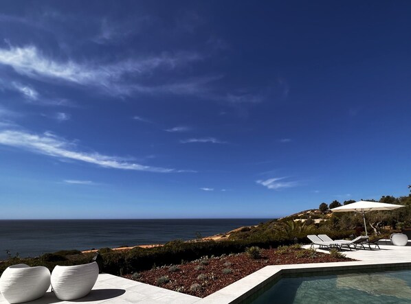 A pool with lounge chairs, a view of the ocean, and a clear sky. - Serene Suite w/ Balcony & Ocean View, Perfect for a Quiet Retreat (Lagos)