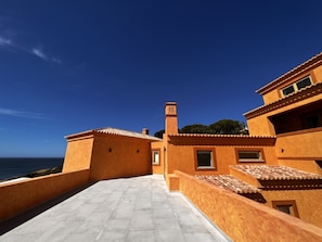 Un edificio costero con terraza, chimenea y vista al mar.