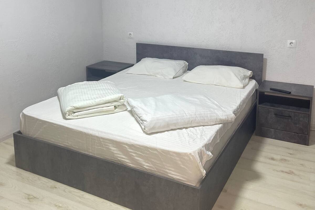 Un dormitori amb un llit, dues taules de nit i una petita taula auxiliar.