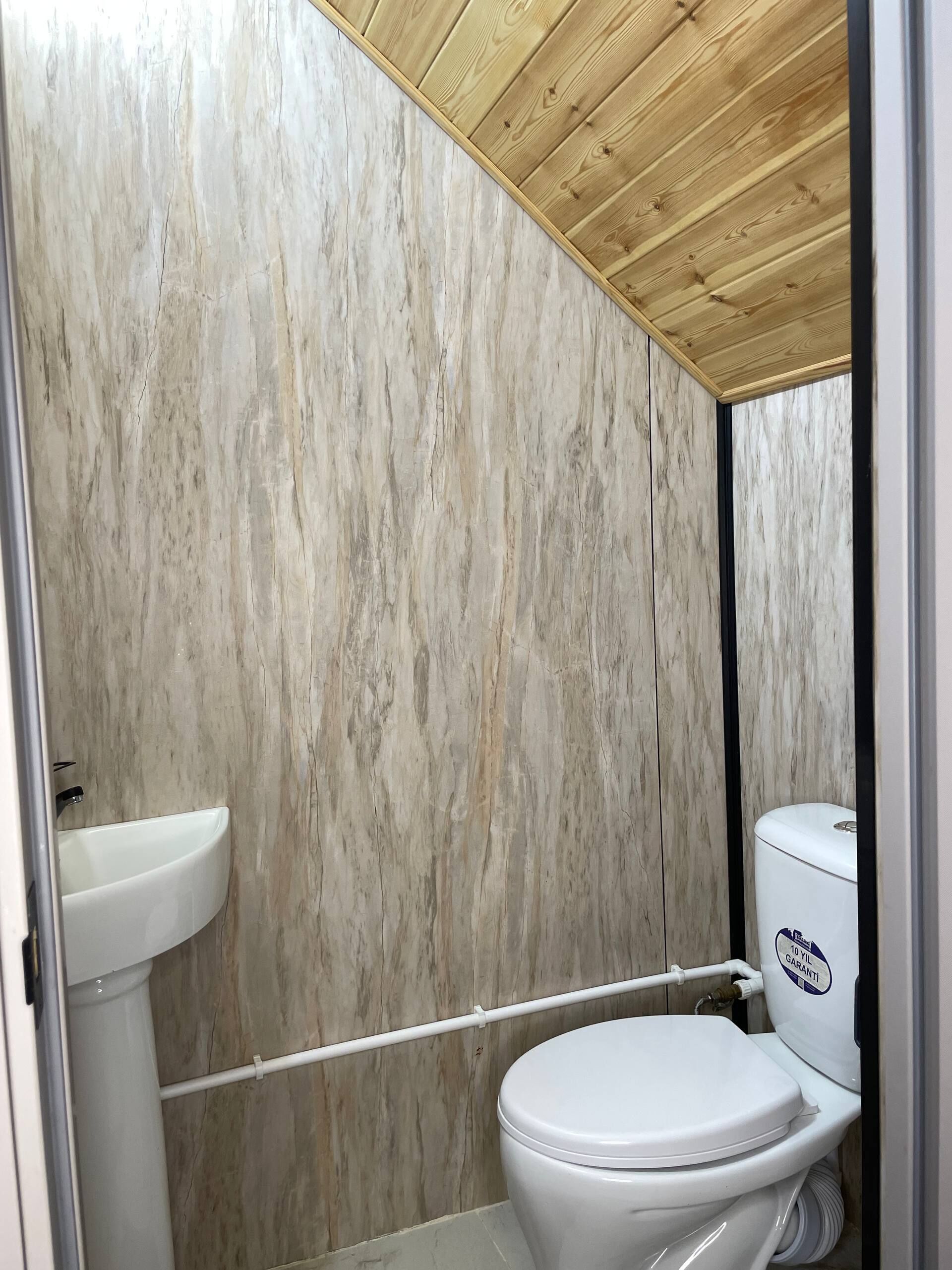 A bathroom with a marble wall, a wooden ceiling, a white sink, and a toilet.