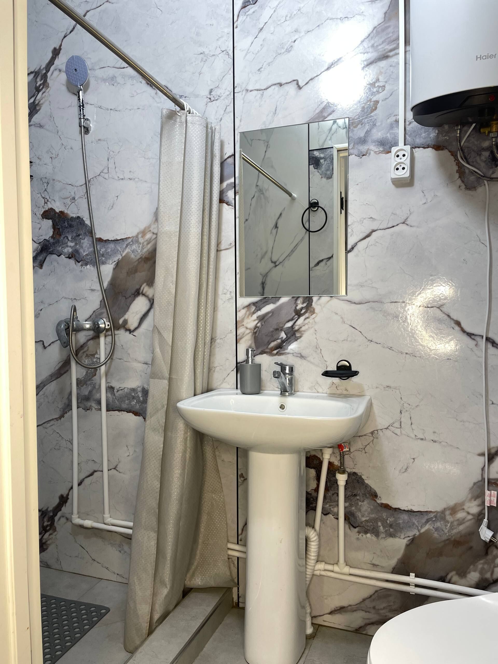 A bathroom with a shower, a sink, a mirror, and marble walls.