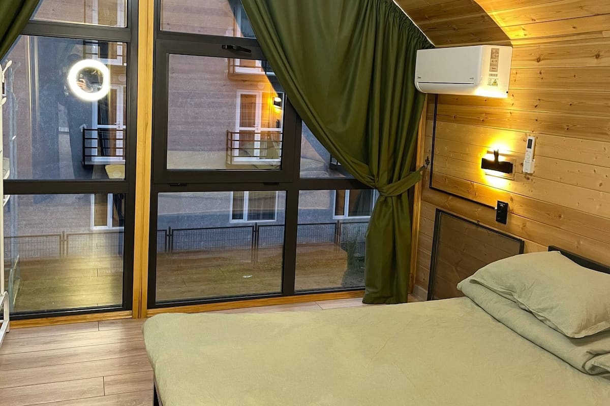 Un dormitori amb un llit, una finestra amb cortines, un aparell d'aire condicionat i vistes a un balcó exterior.