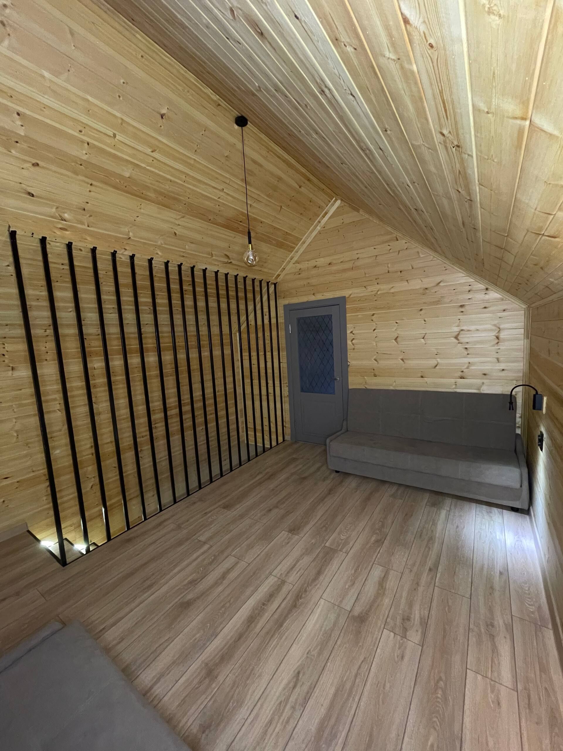 A wooden interior with a sloped ceiling, a sofa, a door, and a light fixture.