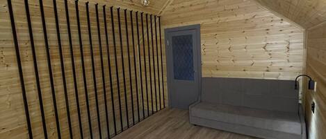 A wooden interior with a sloped ceiling, a sofa, a door, and a light fixture.