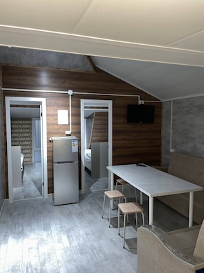 Una cocina compacta con un refrigerador, una mesa de comedor con taburetes y un sofá.