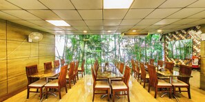 A conference room with a long table, multiple chairs, a ceiling fan, and a view of tropical foliage through large windows.