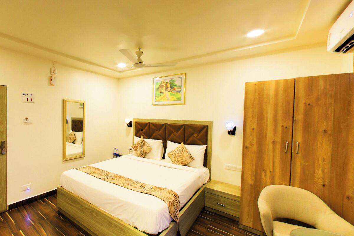 A hotel room with a bed, a wardrobe, a chair, a bedside table, a mirror, and a ceiling fan.