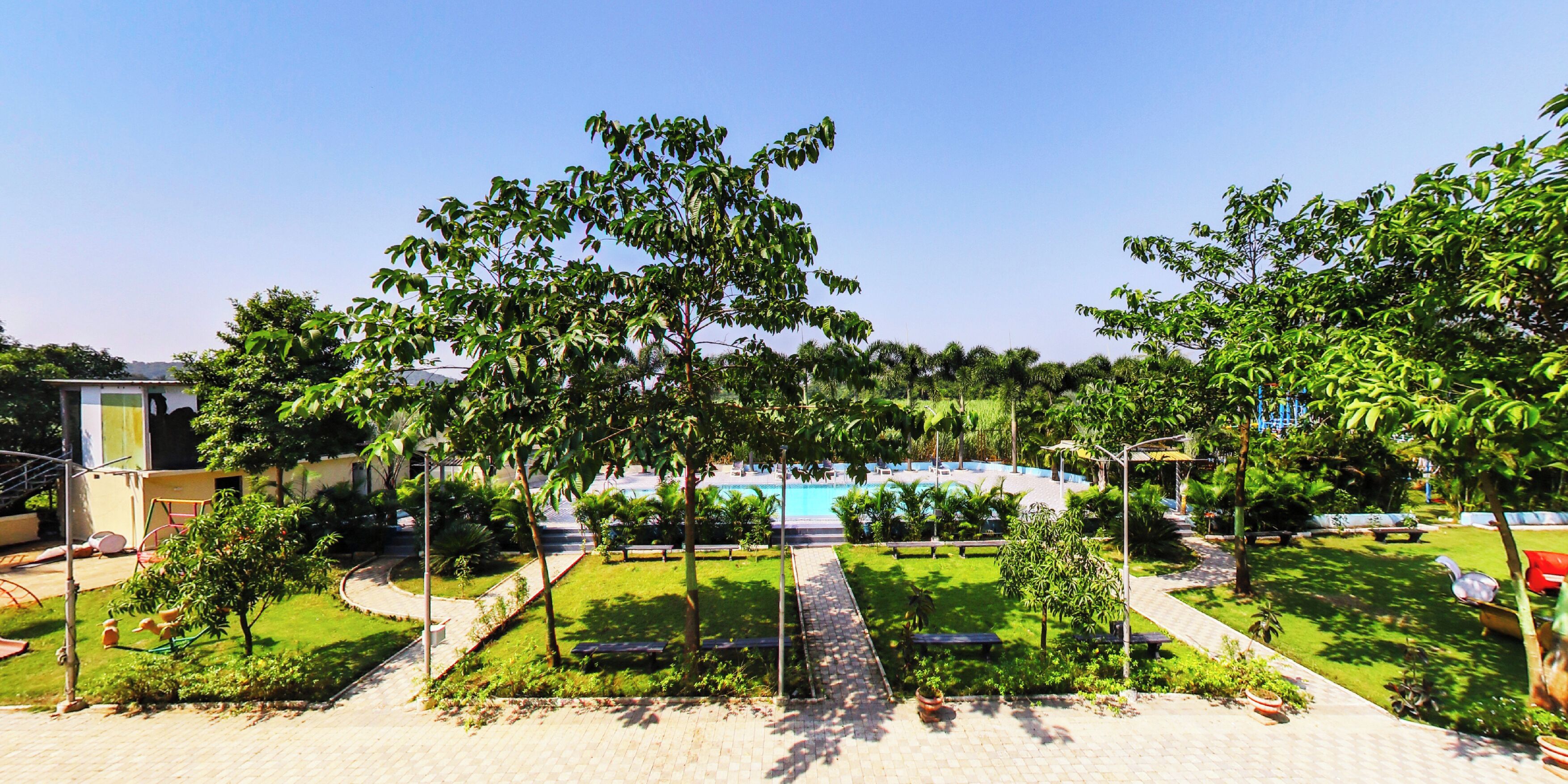 Zona de piscina bajo un cielo despejado, rodeada de vegetación y senderos.