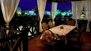 Een terras met een eettafel en stoelen, bedekte gordijnen en lichtslingers.