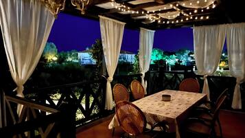 An outdoor dining area with a table and chairs, draped curtains, and string lights.