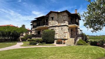 A stone house with a balcony, surrounded by a well-maintained lawn and garden.
