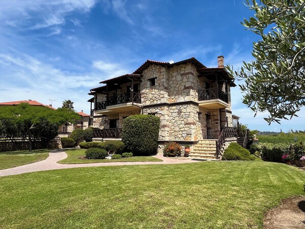Ein Steinhaus mit Balkon, umgeben von einem gepflegten Rasen und Garten.