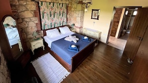 Een slaapkamer met een stenen muur, een bed met een blauwe sprei, een nachtkastje, een dressoir en een spiegel.