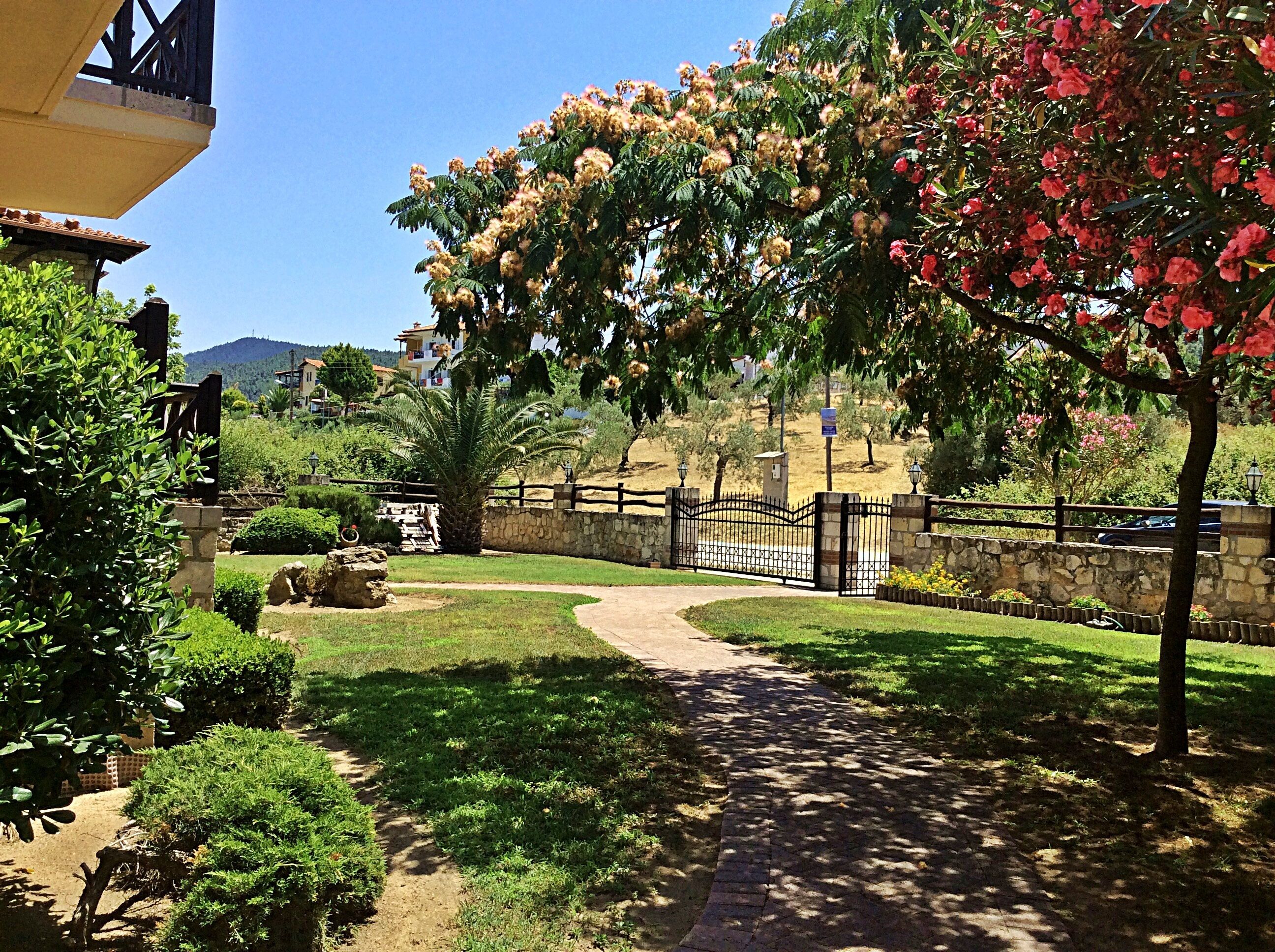 A paved pathway leading through a landscaped area with a stone wall and a metal gate.