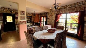 A dining area with a stone wall, a fireplace, wicker chairs, and a chandelier.
