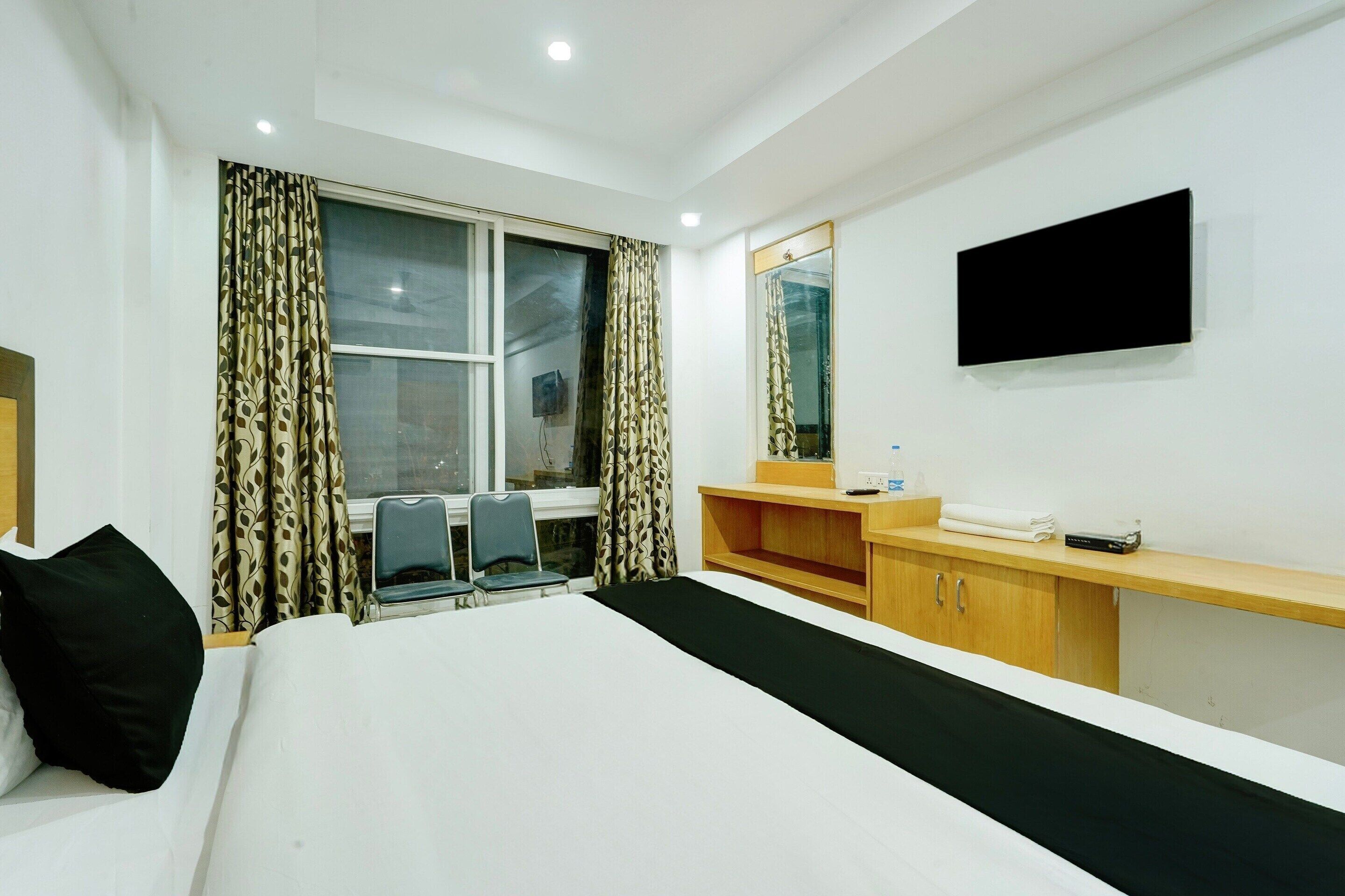 A hotel room with a bed, a desk, a chair, a TV, and a window with curtains.