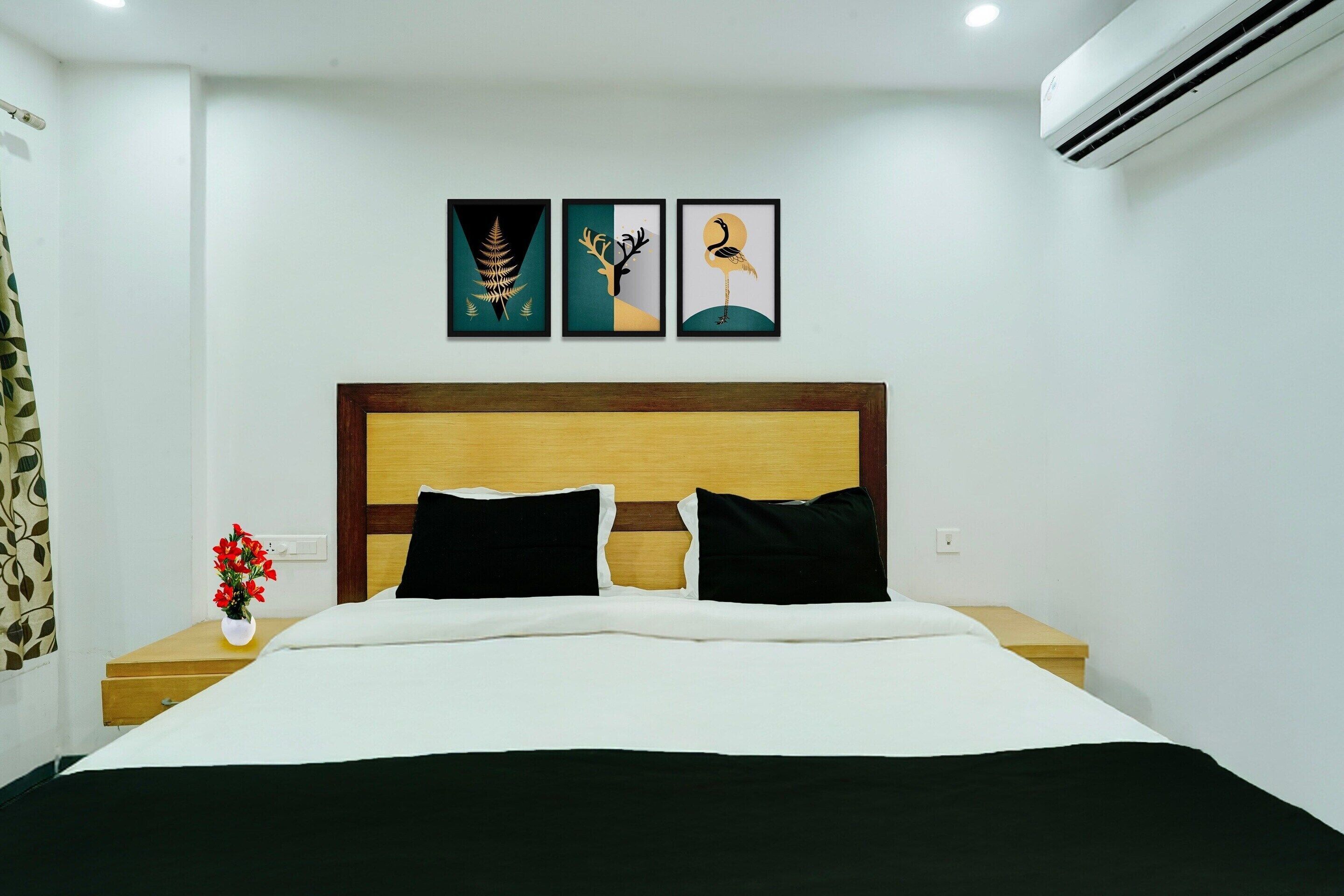 A hotel room with a bed, a nightstand with a vase of flowers, and three framed pictures on the wall.