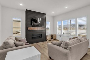 A modern living room with a fireplace, a flat-screen TV, and large windows with a view. - Timpanogos View Retreat with RV Parking Pad (Heber City)