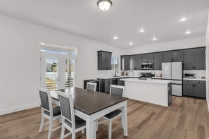 A modern kitchen with dark cabinets, a central island, and a dining area with a table and chairs. - Timpanogos View Retreat with RV Parking Pad (Heber City)