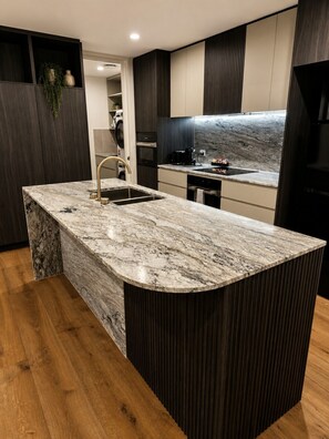 A modern kitchen with a marble island, dark wood cabinetry, and a built-in oven. - Relaxing 2BR with Lake Views in Eastbourne (Parkes)