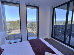A hotel room with a large bed, a view of the landscape, and a balcony with chairs. - Relaxing 2BR with Lake Views in Eastbourne (Parkes)
