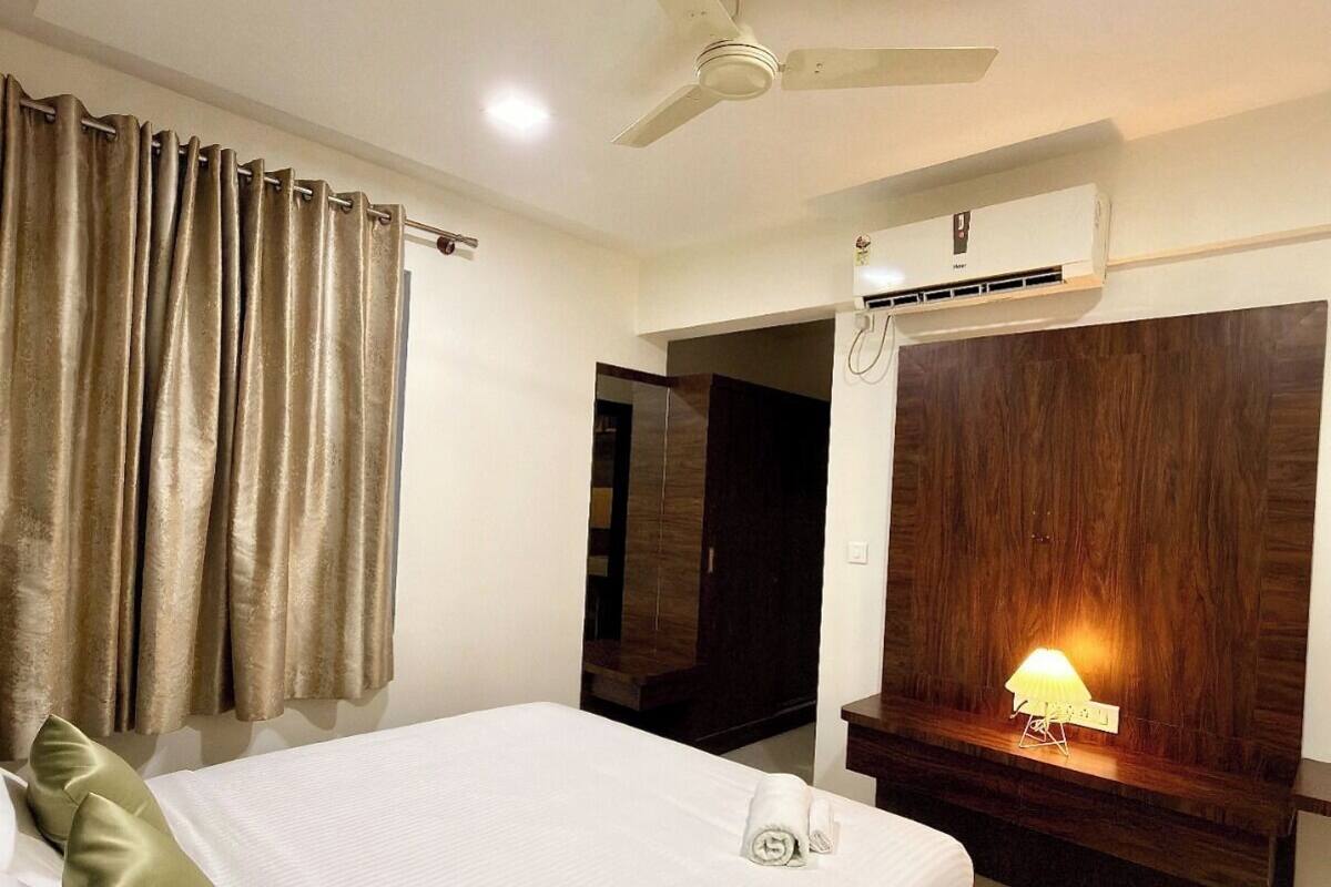 A hotel room with a bed, a ceiling fan, an air conditioning unit, a bedside lamp, and a wooden panel on the wall.