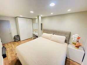 A bedroom with a large bed, a wardrobe, a desk, and a nightstand.